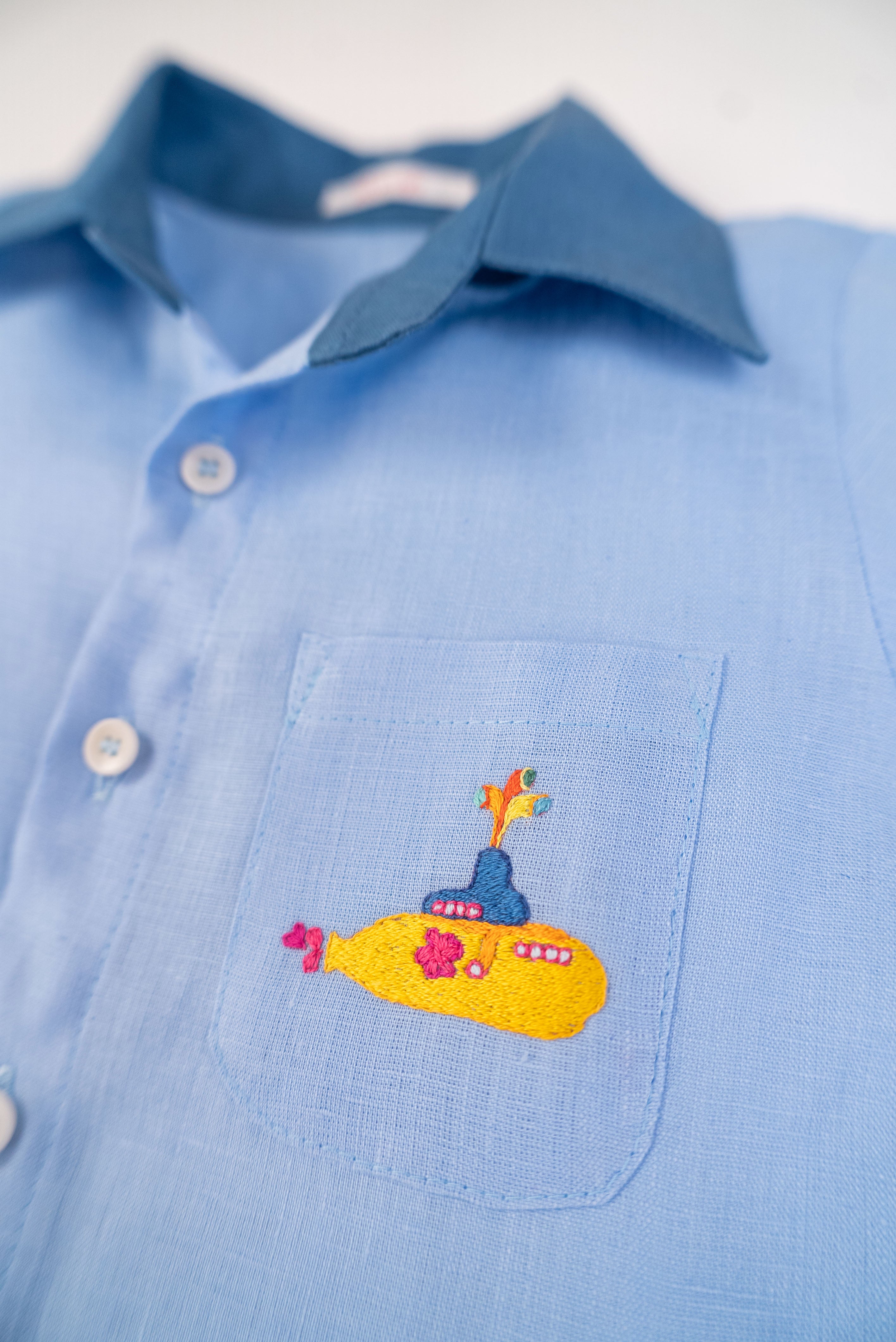 Detalhe do bordado à mão de Yellow Submarine na camisa infantil em linho azul claro