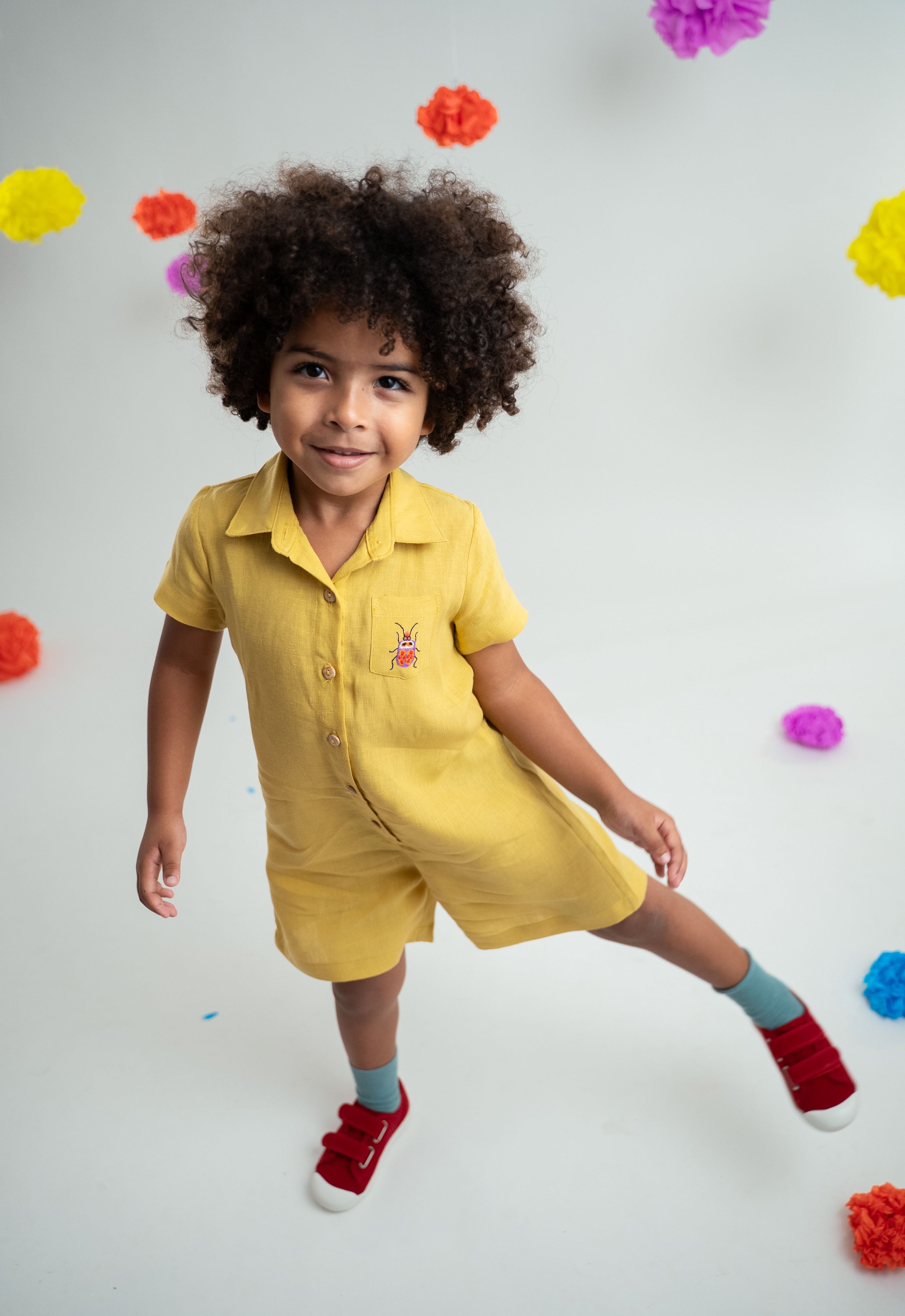 Menino usando macacão infantil unissex em linho amarelo com bordado de besouro.