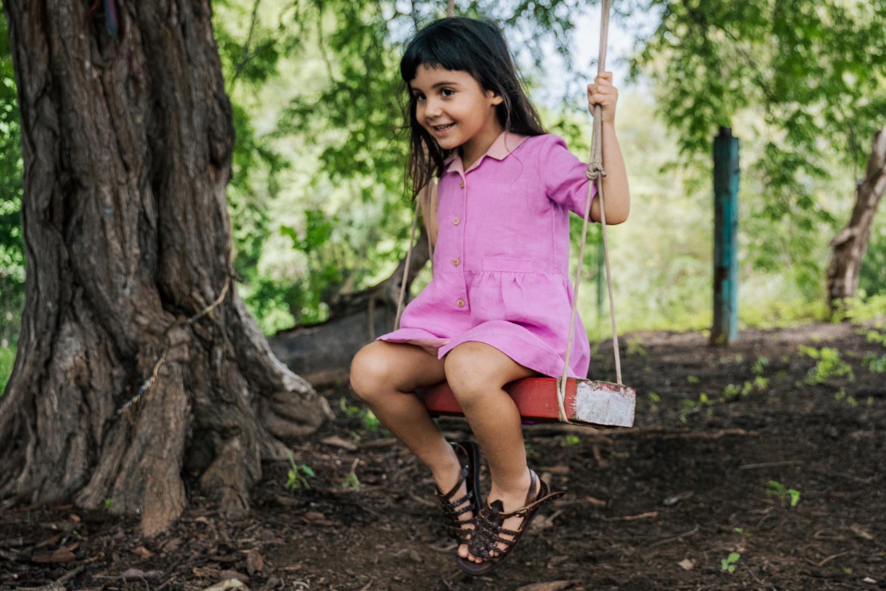 Menina sentada em balanço em jardim usando vestido rosa de linho puro