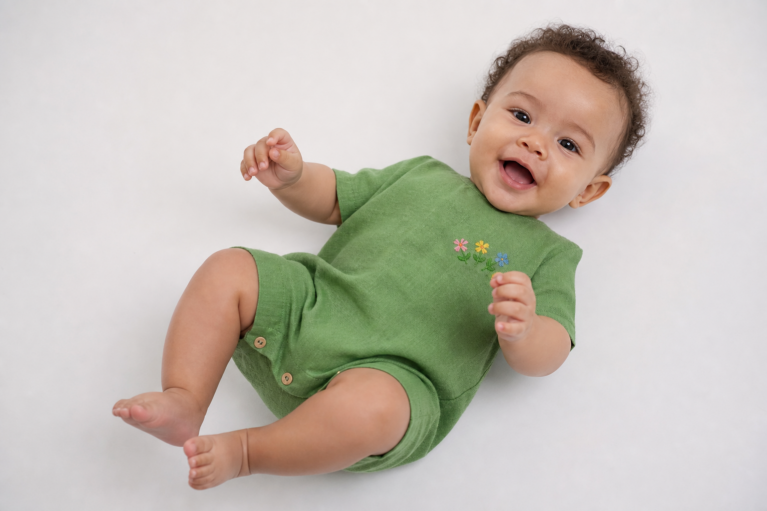 Bebê deitado em estúdio vestindo macacão de linho verde-folha com bordado à mão de flores miúdas