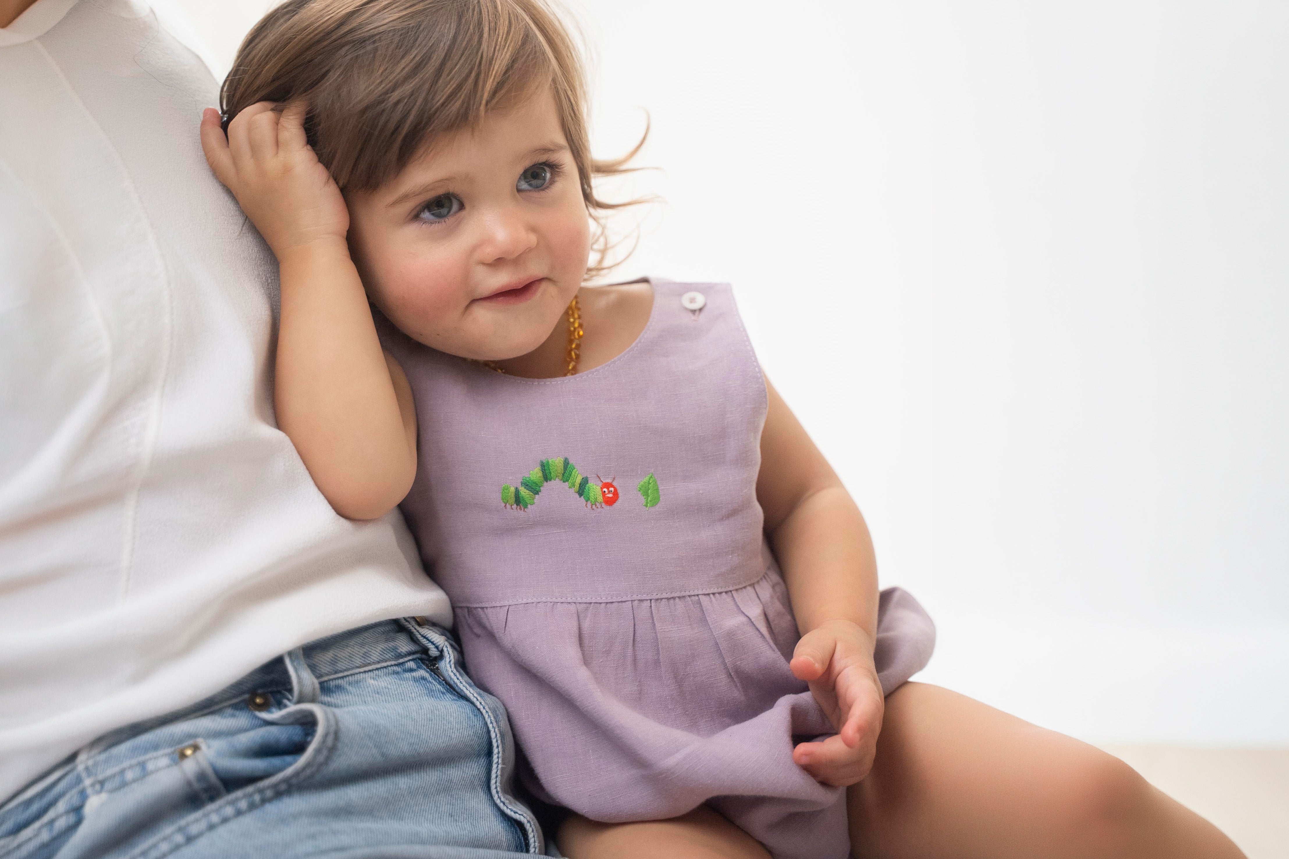 Bebê no colo usando vestido lilás de linho bordado em ensaio de acompanhamento