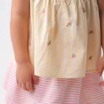 Detalhe de menina vestindo Bata Flora infantil em algodão anarruga listrado amarelo com flores rosas bordadas à mão