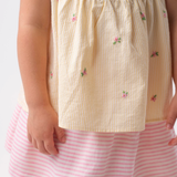Detalhe de menina vestindo Bata Flora infantil em algodão anarruga listrado amarelo com flores rosas bordadas à mão