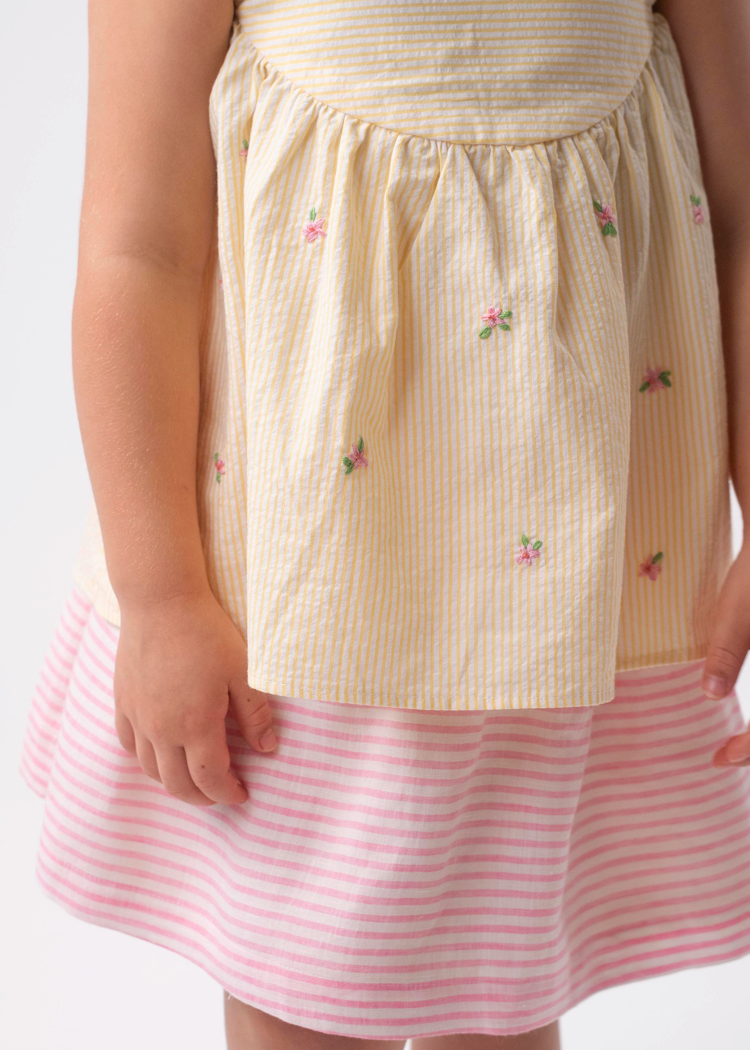 Detalhe de menina vestindo Bata Flora infantil em algodão anarruga listrado amarelo com flores rosas bordadas à mão