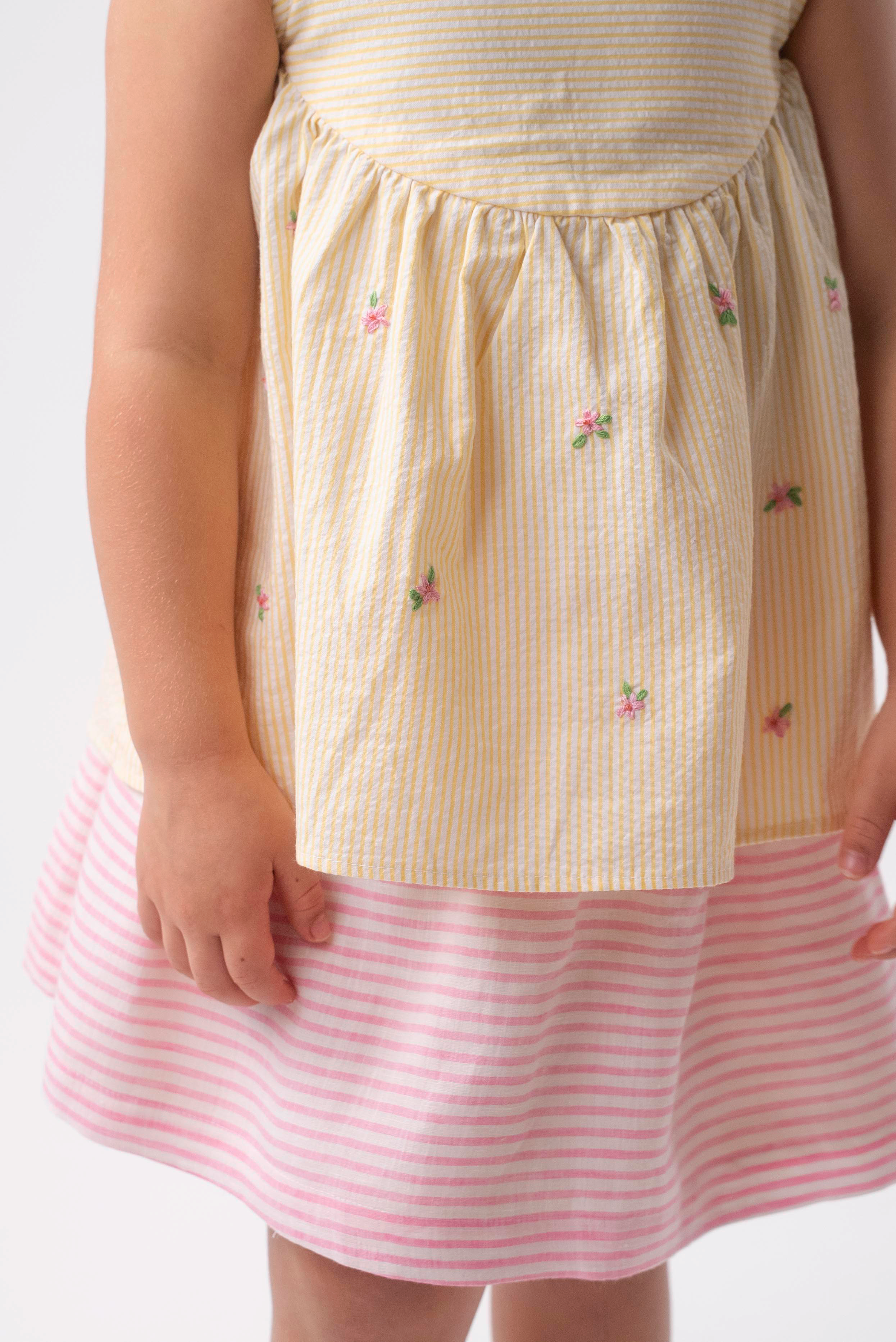 Detalhe de menina vestindo Bata Flora infantil em algodão anarruga listrado amarelo com flores rosas bordadas à mão