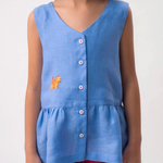 Menina vestindo Bata Lola infantil azul em 100% linho com decote V, botões frontais e bordado à mão, combinando com shorts vinho