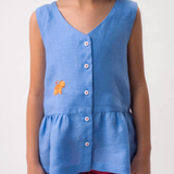 Menina vestindo Bata Lola infantil azul em 100% linho com decote V, botões frontais e bordado à mão, combinando com shorts vinho