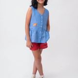 Menina usando Bata Lola infantil em linho azul com bordado de capivara e shorts vermelho