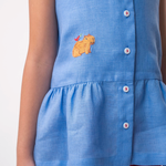 Detalhe de menina usando Bata Lola infantil em linho azul com bordado de capivara e barra franzida