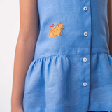 Detalhe de menina usando Bata Lola infantil em linho azul com bordado de capivara e barra franzida