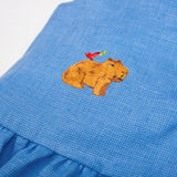 Detalhe da Bata Lola infantil em linho azul com capivara e passarinho bordados à mão