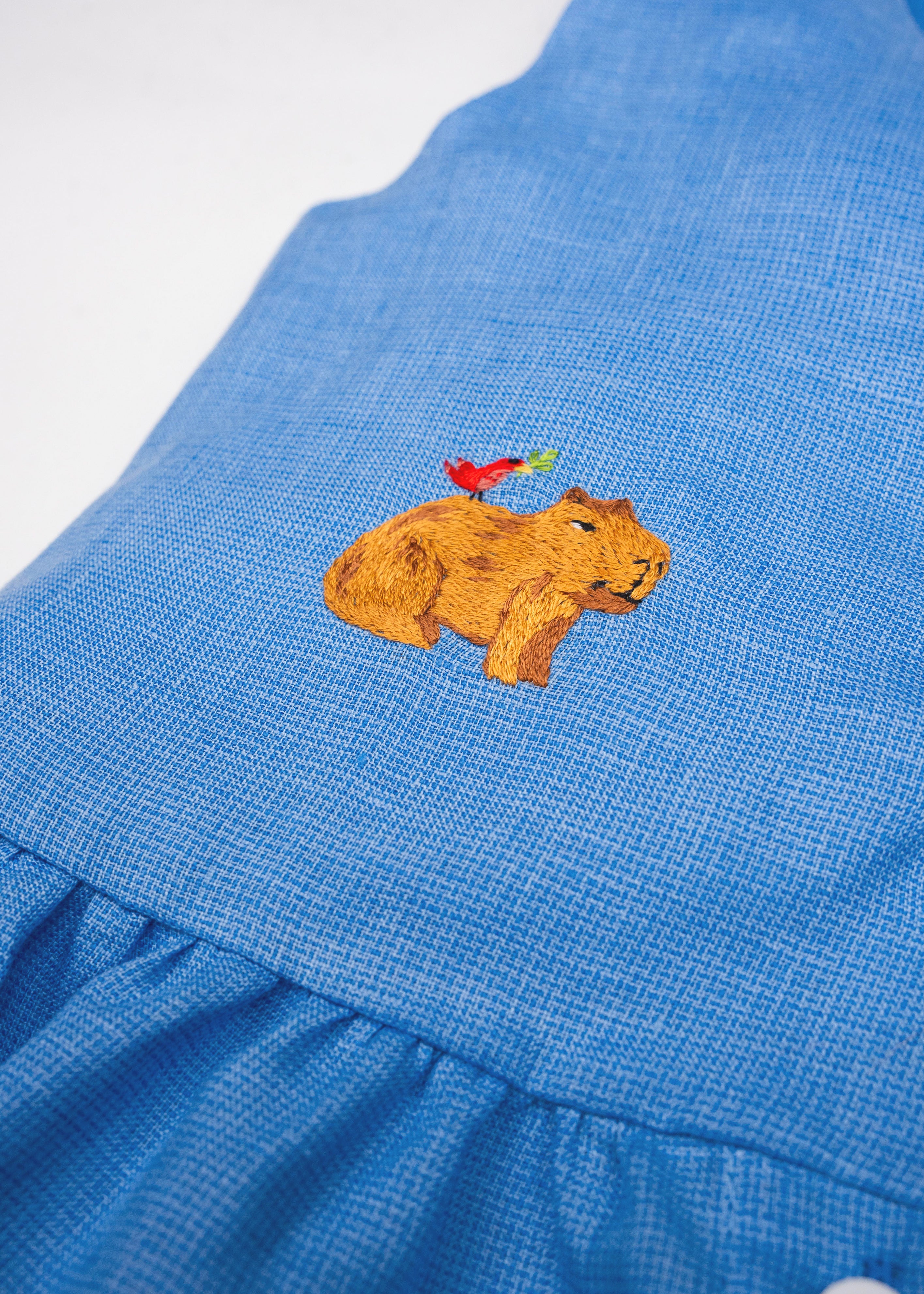 Detalhe da Bata Lola infantil em linho azul com capivara e passarinho bordados à mão