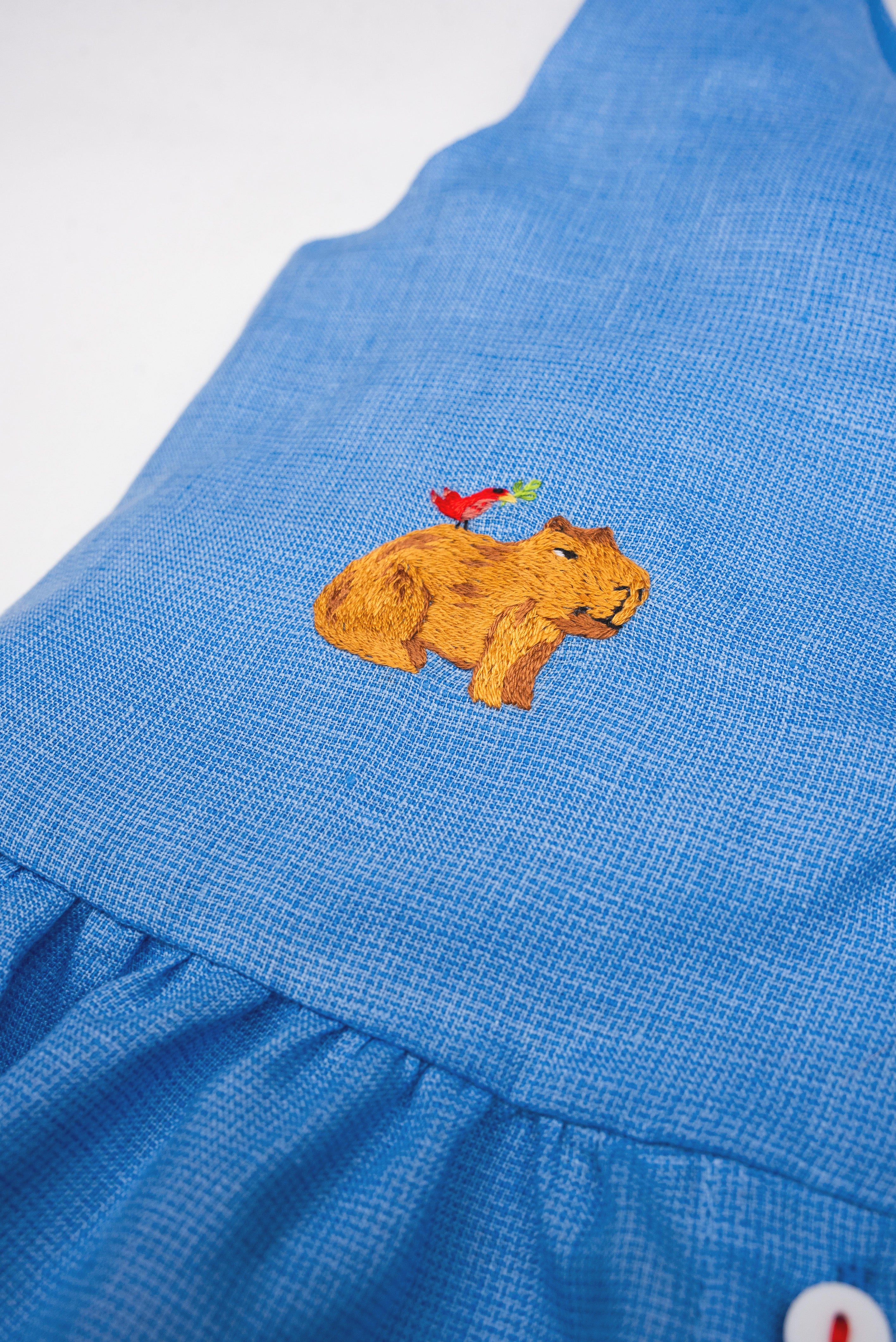 Detalhe da Bata Lola infantil em linho azul com capivara e passarinho bordados à mão