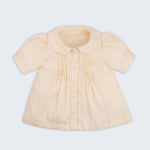Bata infantil de menina off-while com mangas curtas levemente bufantes, gola Peter Pan arredondada e pregas no peitilho, vista de frente.