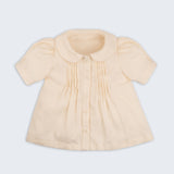 Bata infantil de menina off-while com mangas curtas levemente bufantes, gola Peter Pan arredondada e pregas no peitilho, vista de frente.
