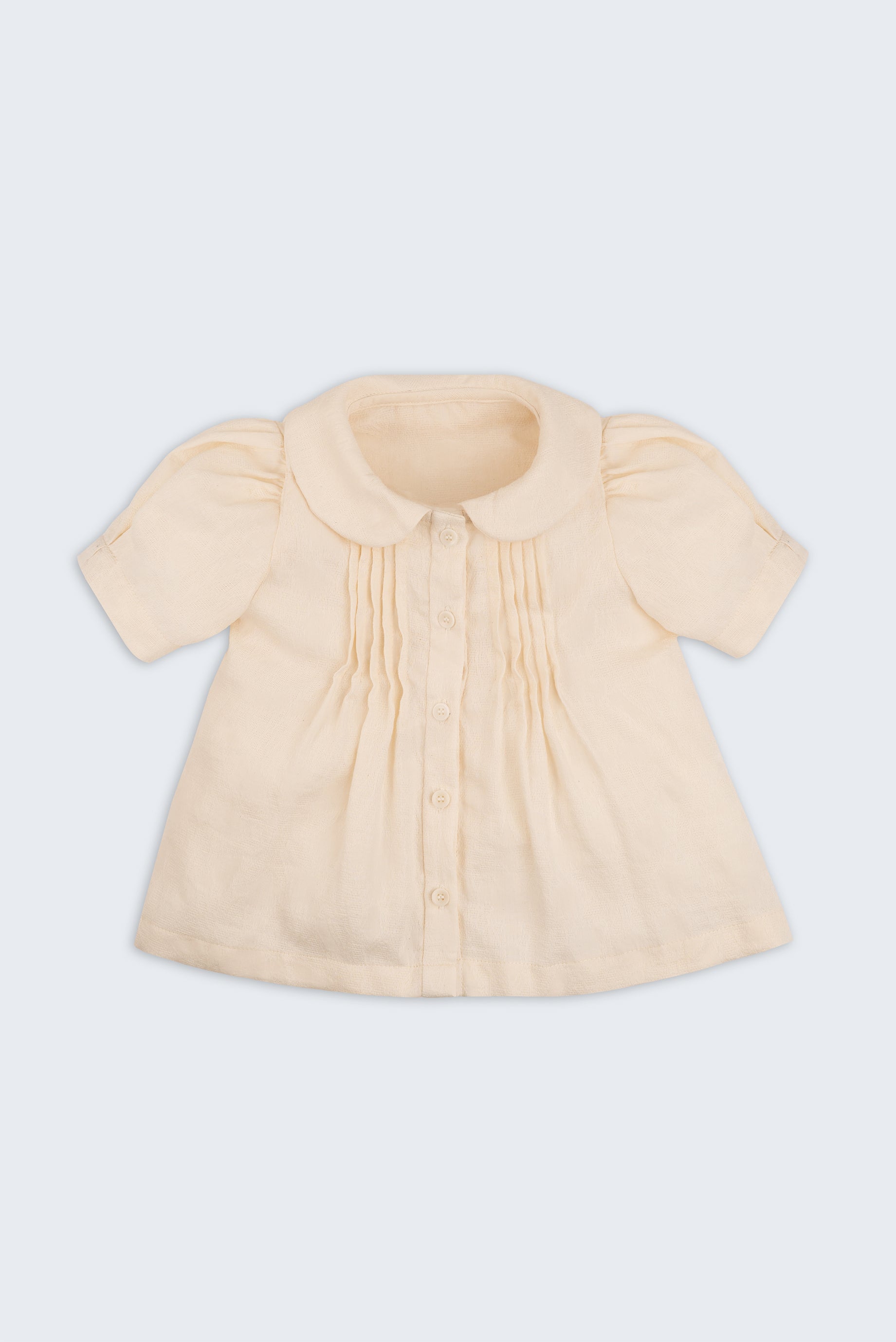 Bata infantil de menina off-while com mangas curtas levemente bufantes, gola Peter Pan arredondada e pregas no peitilho, vista de frente.