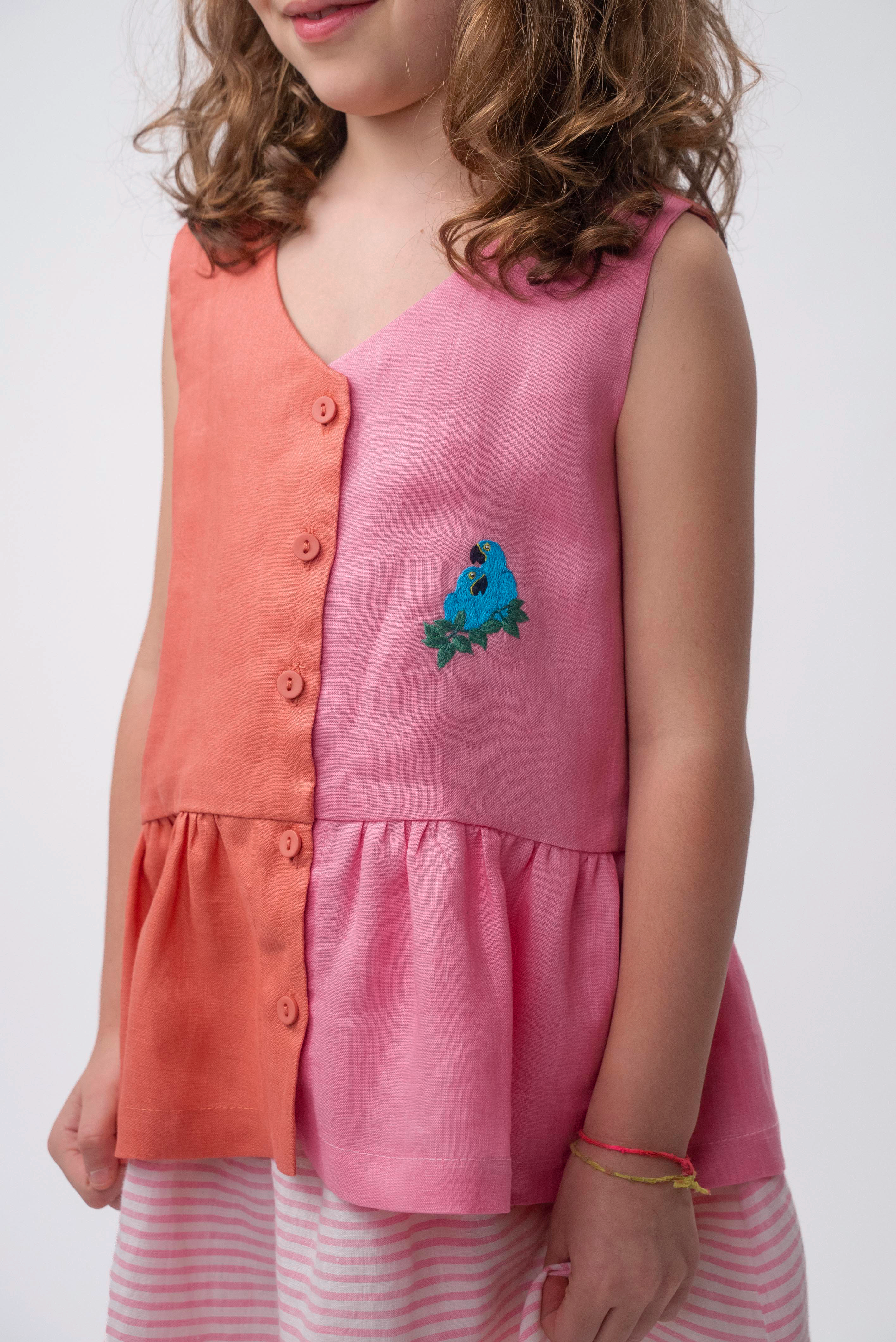 Detalhe da Bata Lola vestida, com decote em V, abotoamento frontal, combinação rosa e coral e bordado de araras.