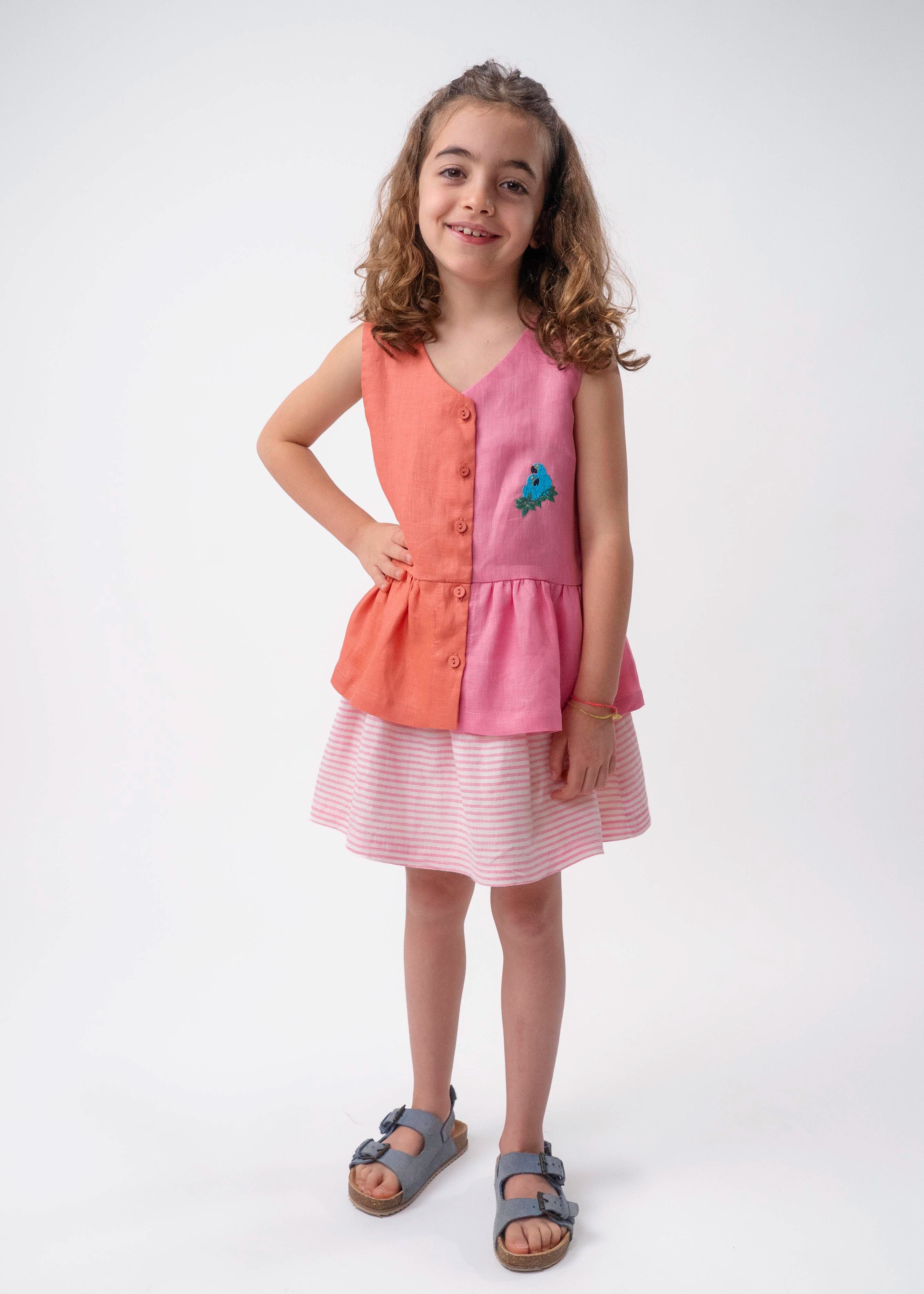Menina usando Bata Lola infantil em linho bicolor rosa e coral com bordado de araras-azuis