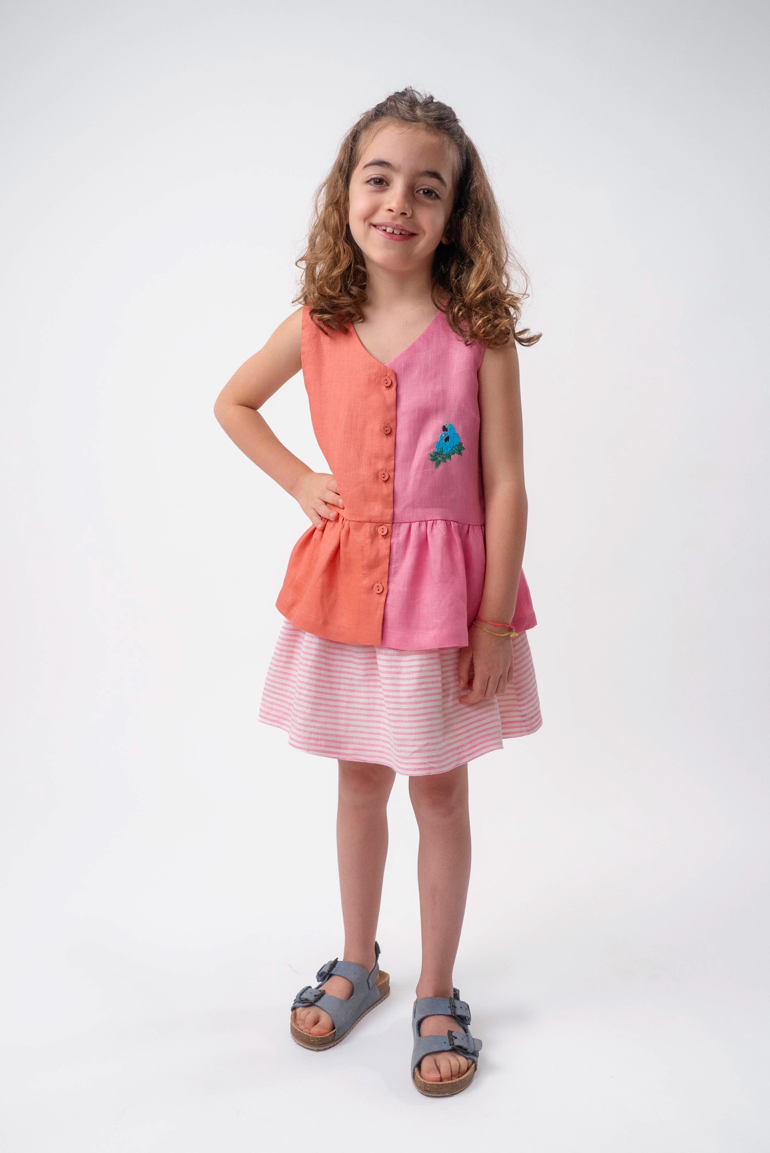 Menina usando Bata Lola infantil em linho bicolor rosa e coral com bordado de araras-azuis
