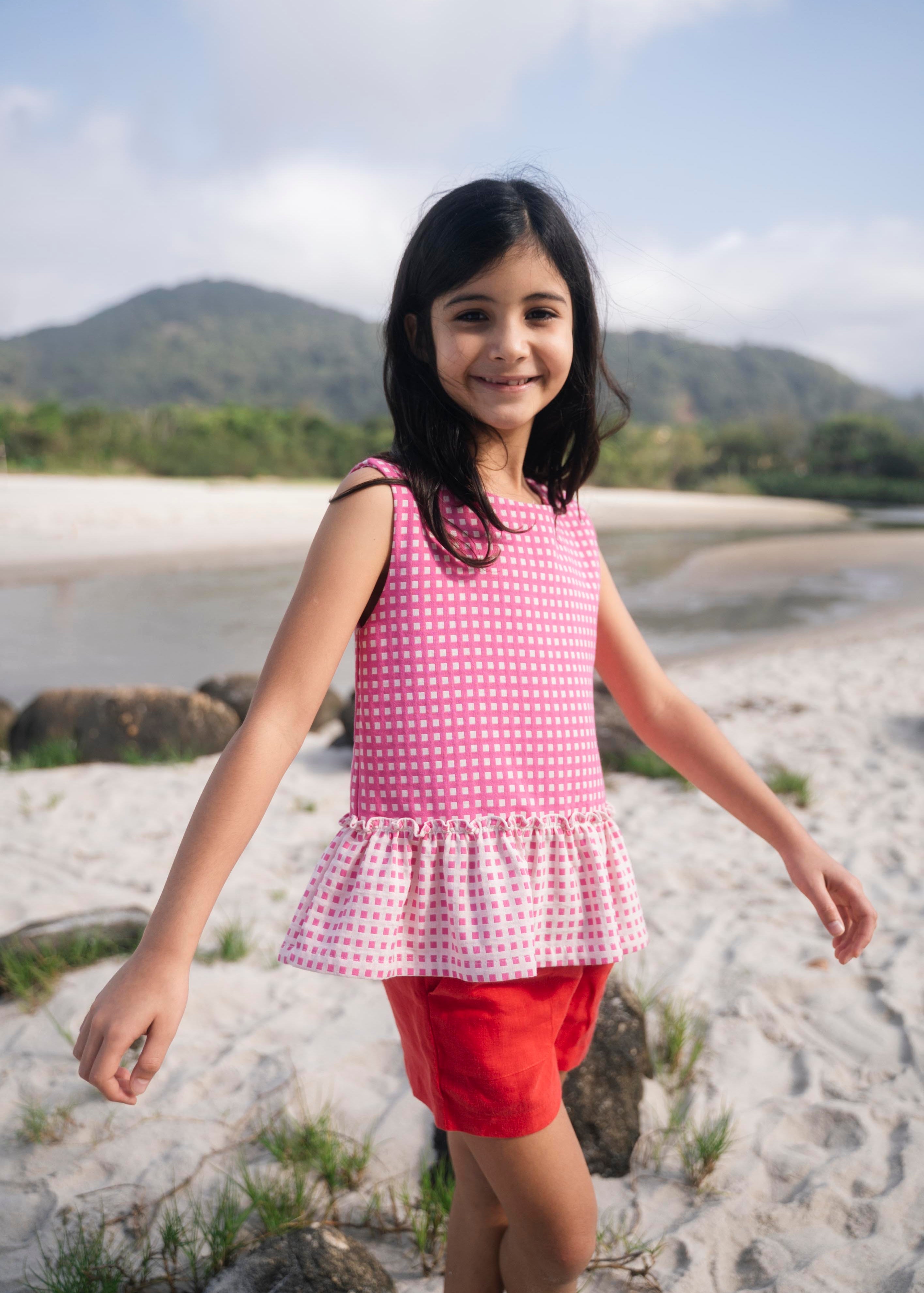 Menina usando bata com estampa xadrez vichy rosa e barra drapeada com babado em padrão invertido.