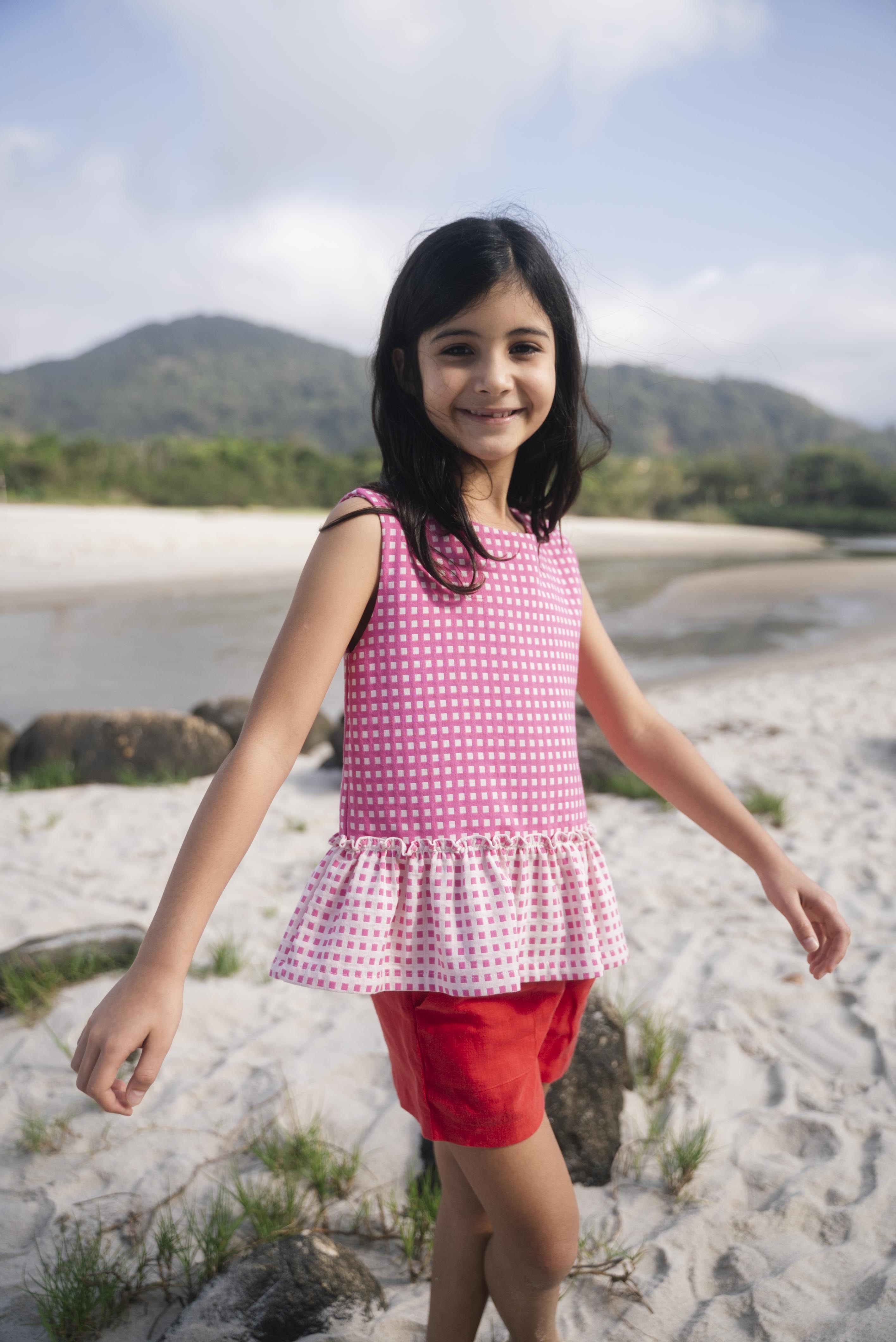 Menina usando bata com estampa xadrez vichy rosa e barra drapeada com babado em padrão invertido.