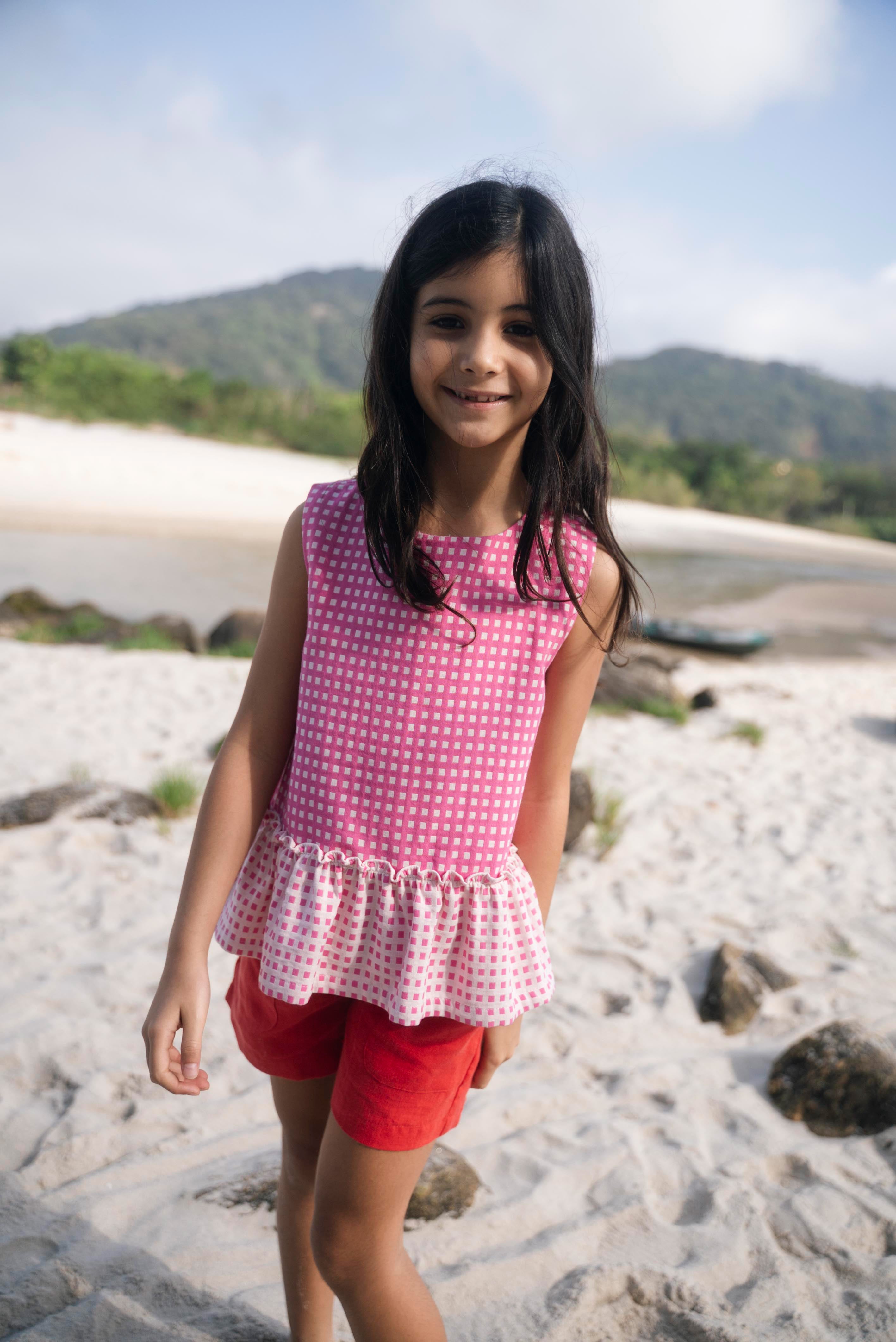 Menina usando bata com estampa xadrez vichy rosa e barra drapeada com babado.