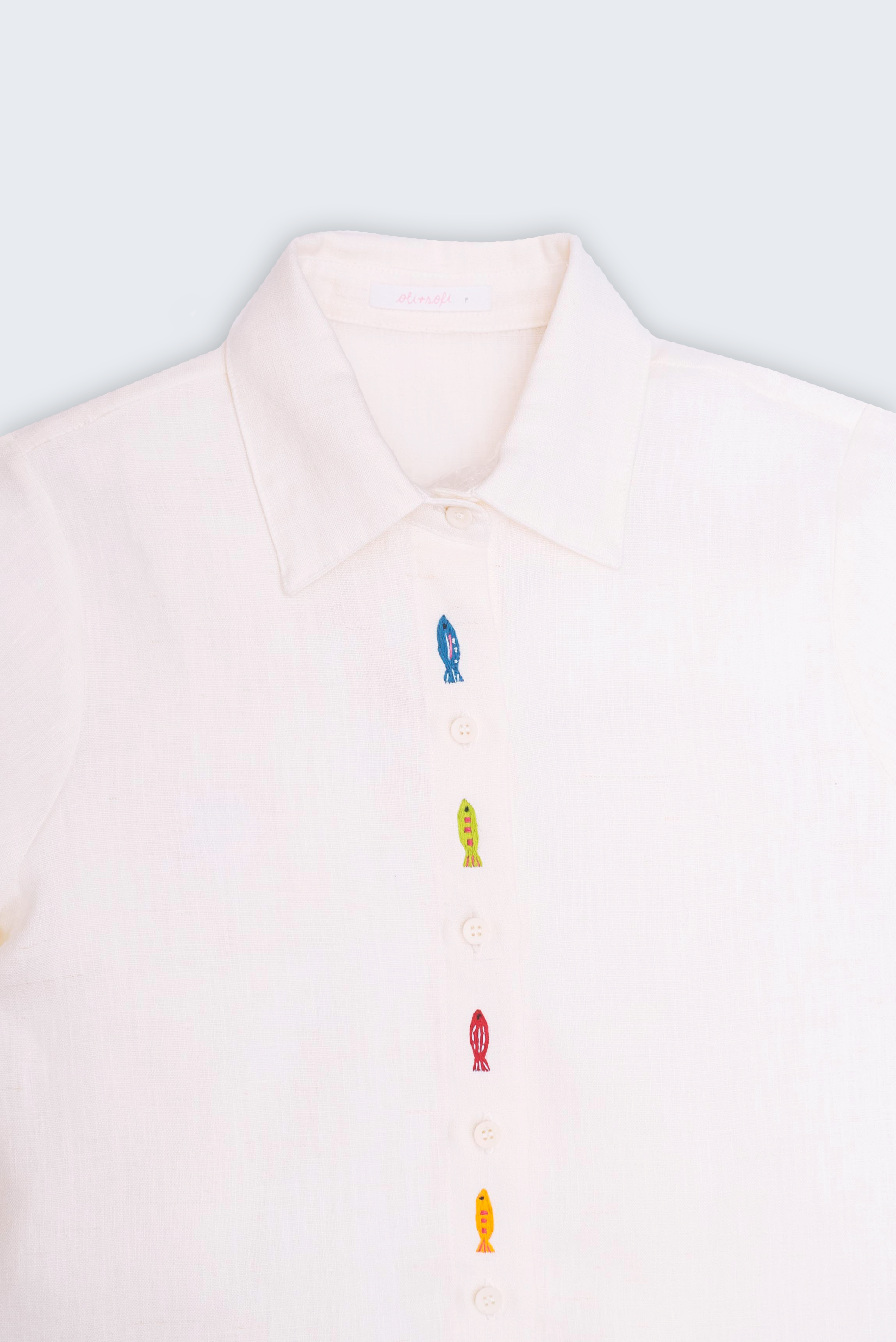 Detalhe da gola e bordados de peixes coloridos em camisa feminina de linho branco Oli e Sofi