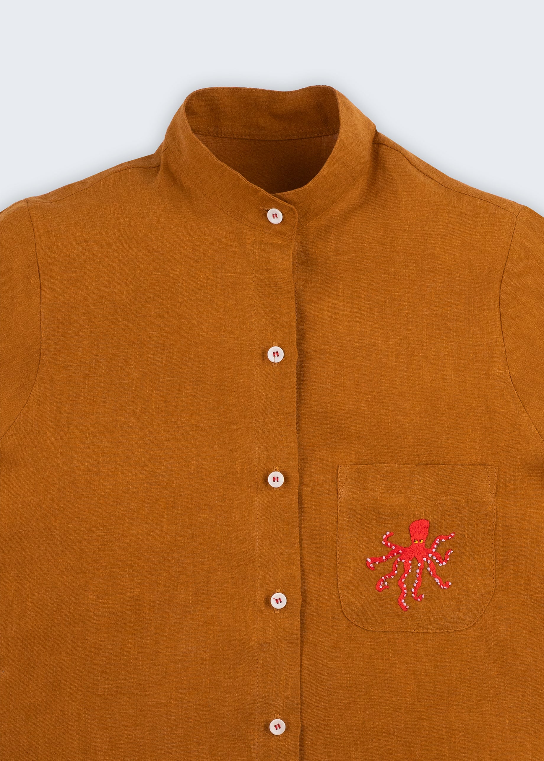 Camisa feminina adulto em linho puro terracota com gola padre, bolso bordado à mão com polvo vermelho e botões brancos, vista em detalhe.