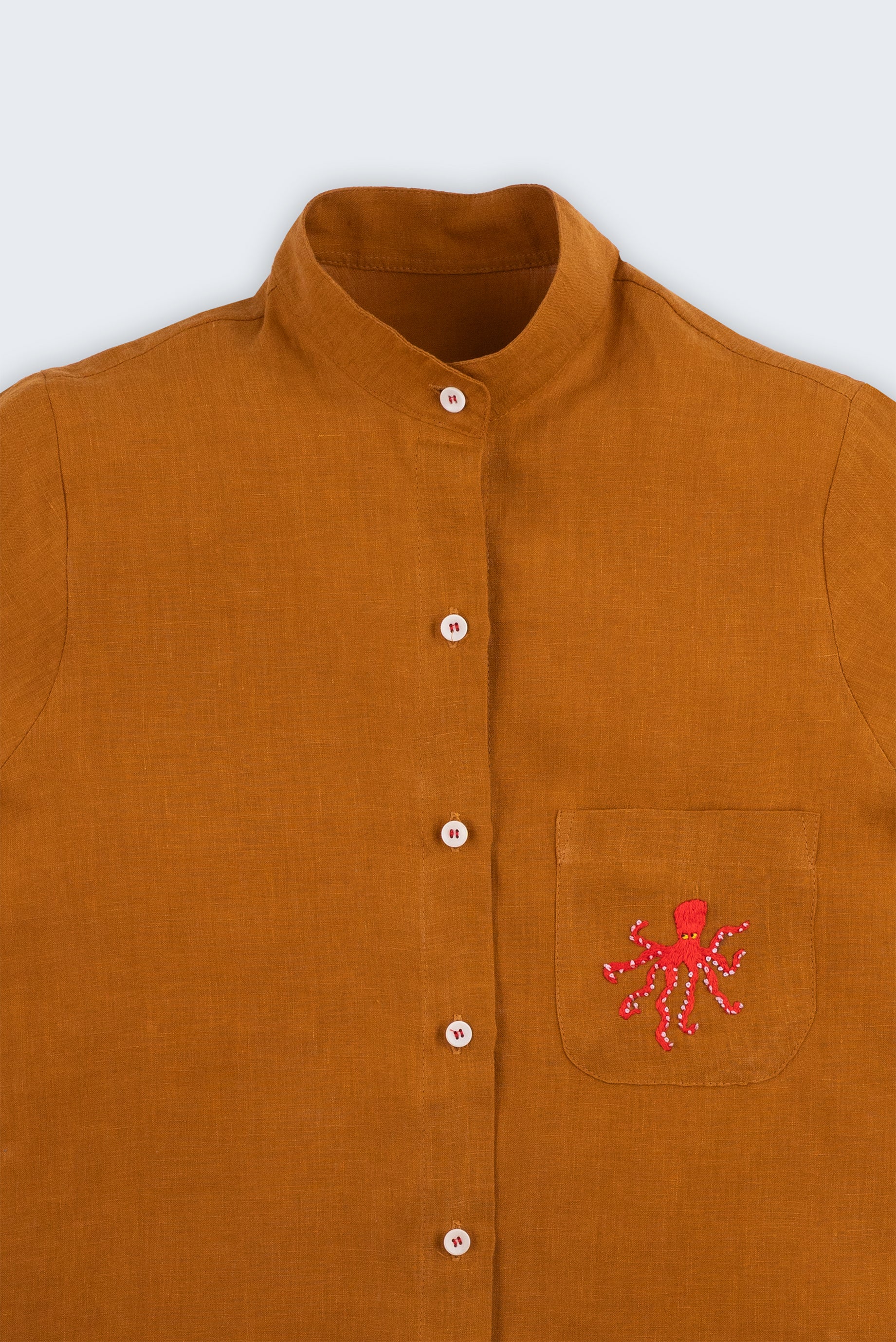 Camisa feminina adulto em linho puro terracota com gola padre, bolso bordado à mão com polvo vermelho e botões brancos, vista em detalhe.
