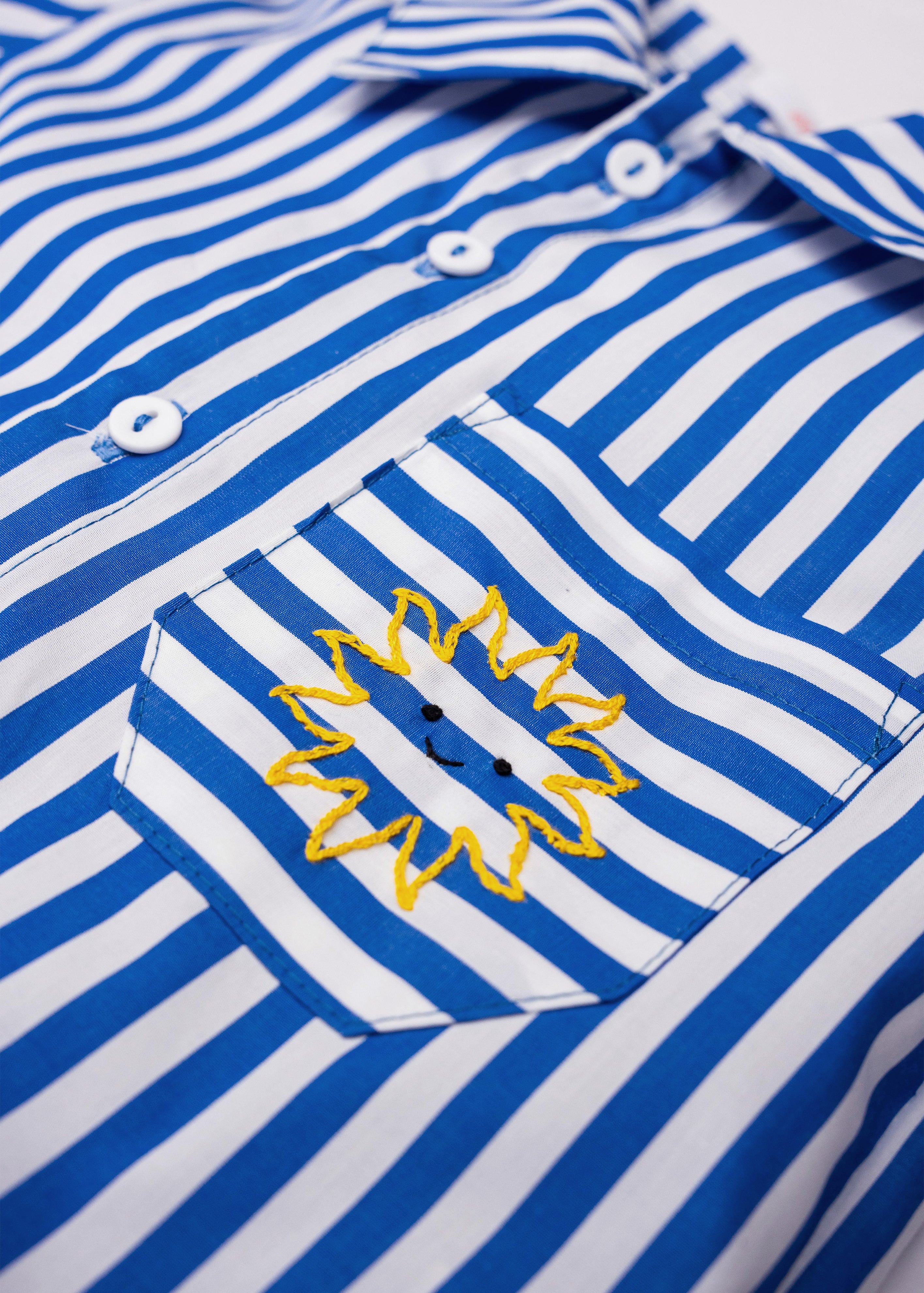 Detalhe do bolso da Camisa Gil em algodão listrado azul e branco com sol amarelo bordado à mão.