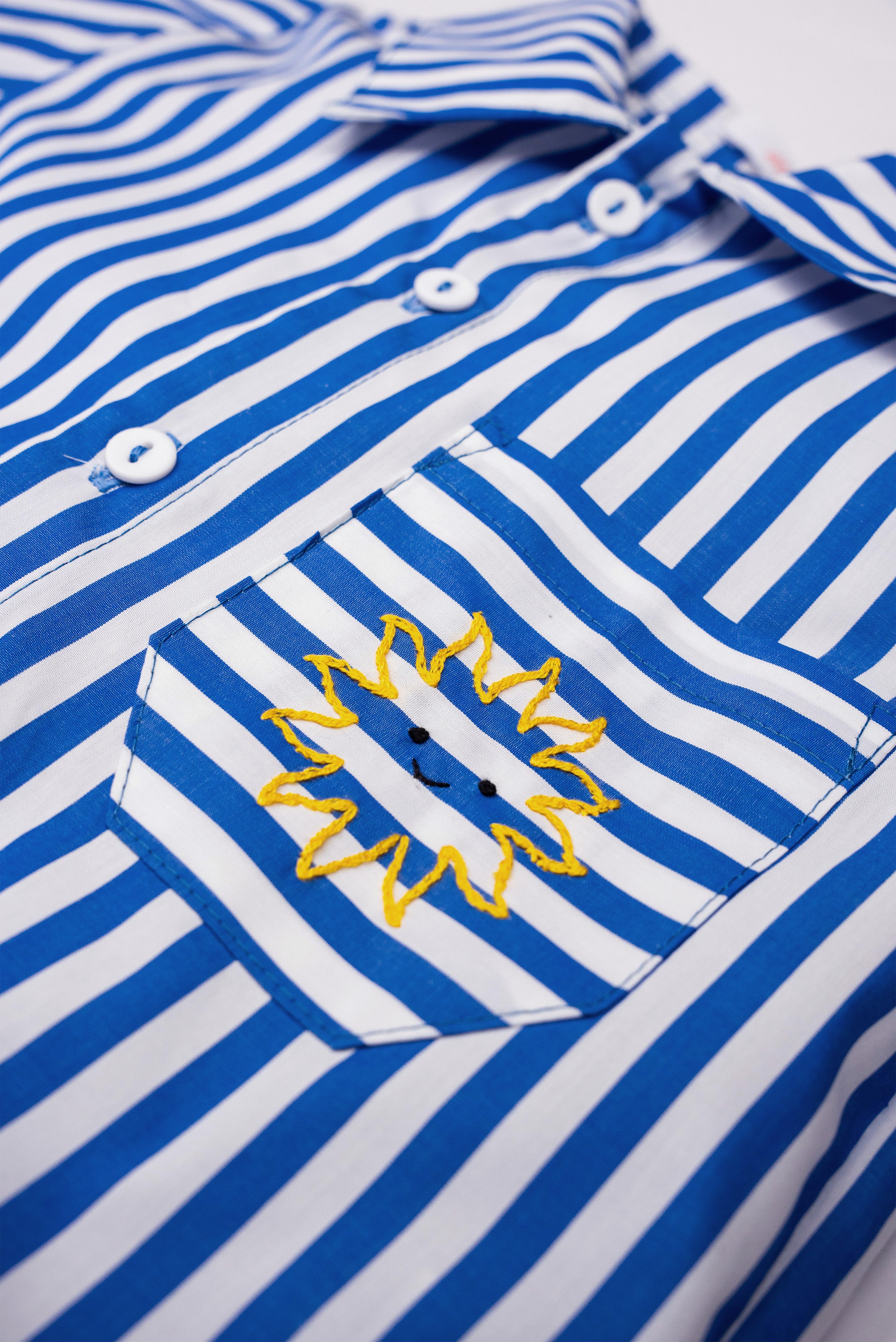 Detalhe do bolso da Camisa Gil em algodão listrado azul e branco com sol amarelo bordado à mão.
