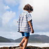 Menino de costas com camisa infantil listrada azul em algodão.