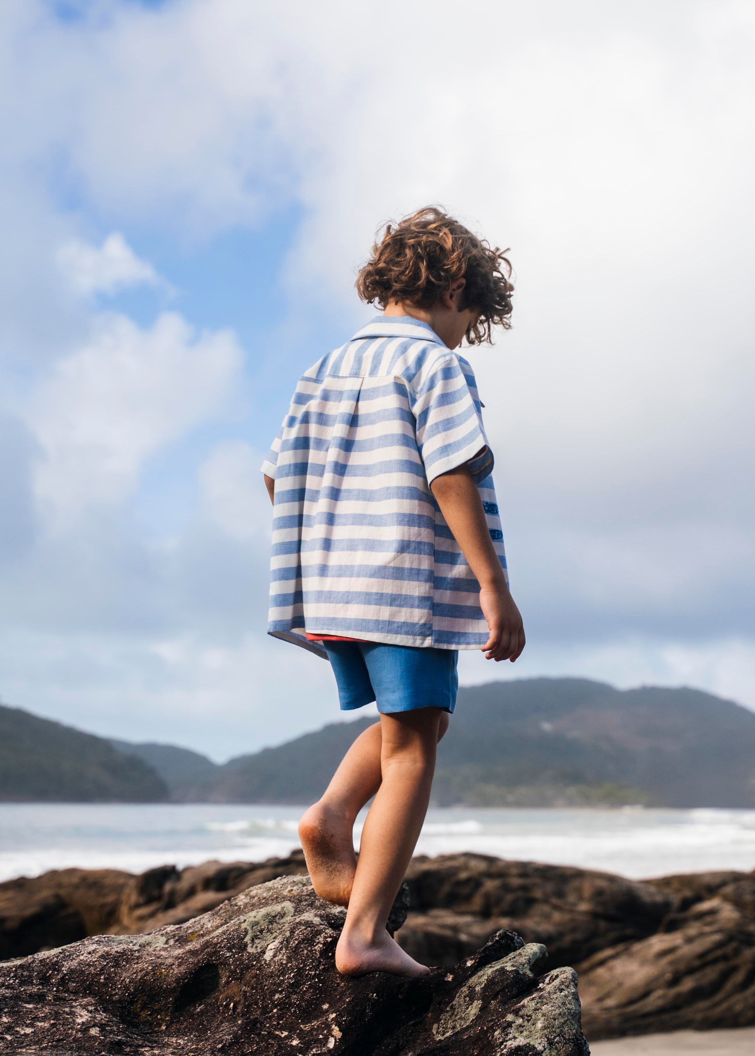 Menino de costas com camisa infantil listrada azul em algodão.