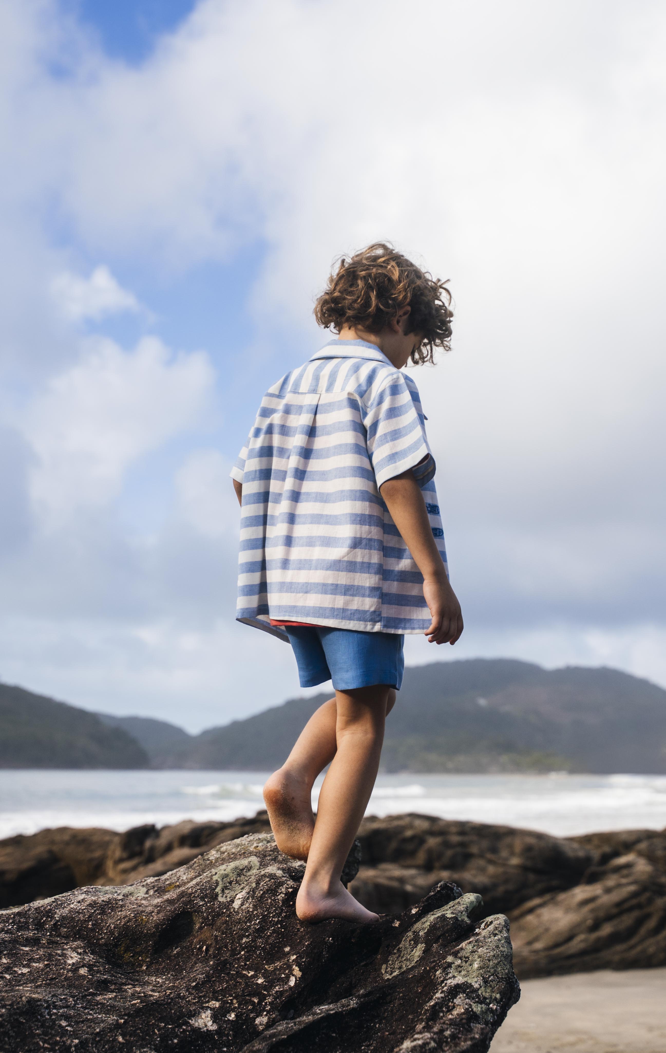 Menino de costas com camisa infantil listrada azul em algodão.
