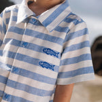 Close de menino com camisa infantil listrada azul em algodão com peixes bordados.