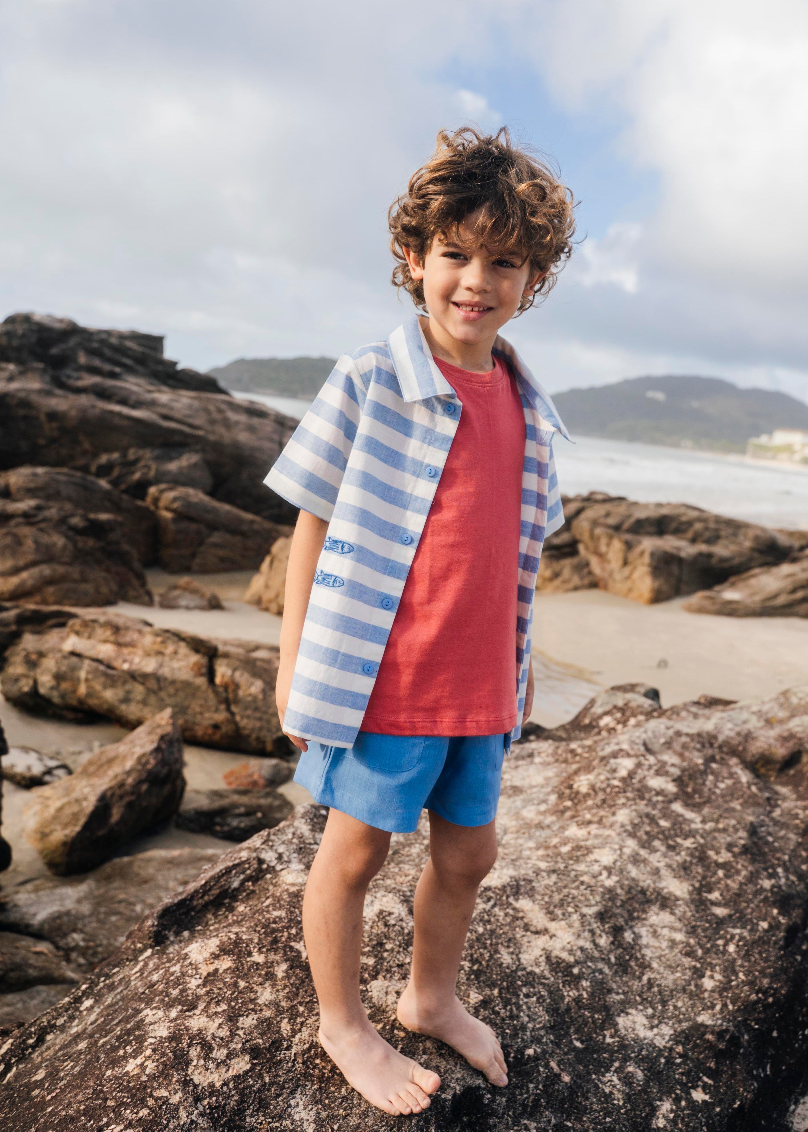 Menino com camisa infantil listrada azul em com peixes bordados, em sobreposição de camiseta.