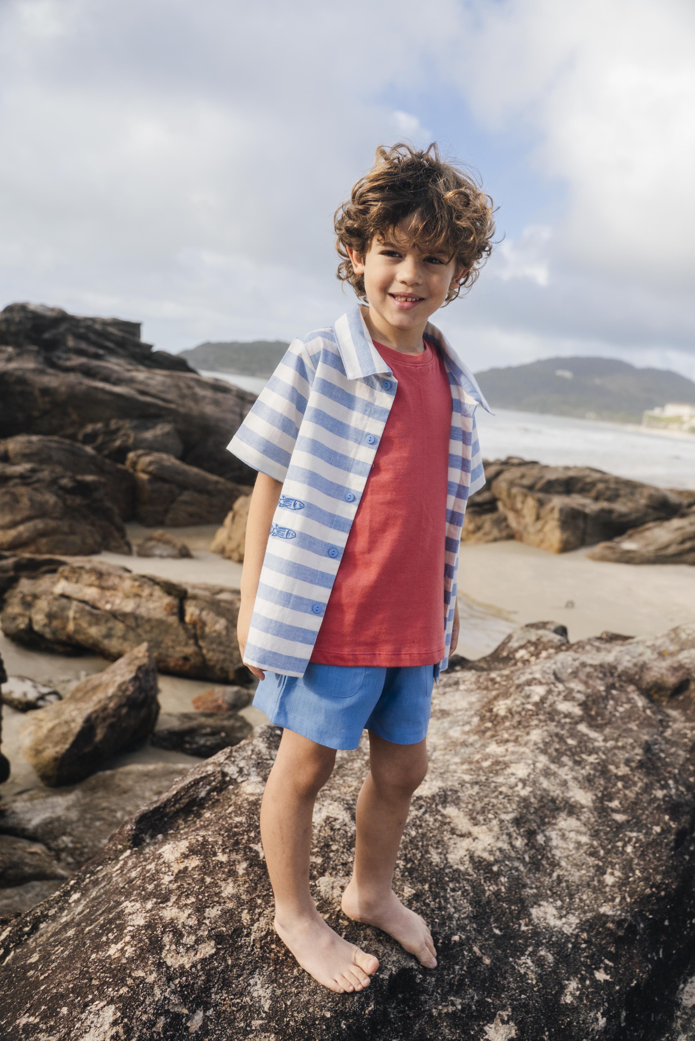 Menino com camisa infantil listrada azul em com peixes bordados, em sobreposição de camiseta.