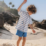 Menino com camisa infantil listrada azul em algodão BCI com peixes bordados e shorts azul combinando.