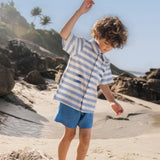 Menino com camisa infantil listrada azul em algodão BCI com peixes bordados e shorts azul combinando.