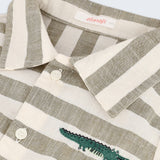 Detalhe da camisa infantil listrada verde oliva e off-white com bordado à mão de jacaré no peito e botões brancos