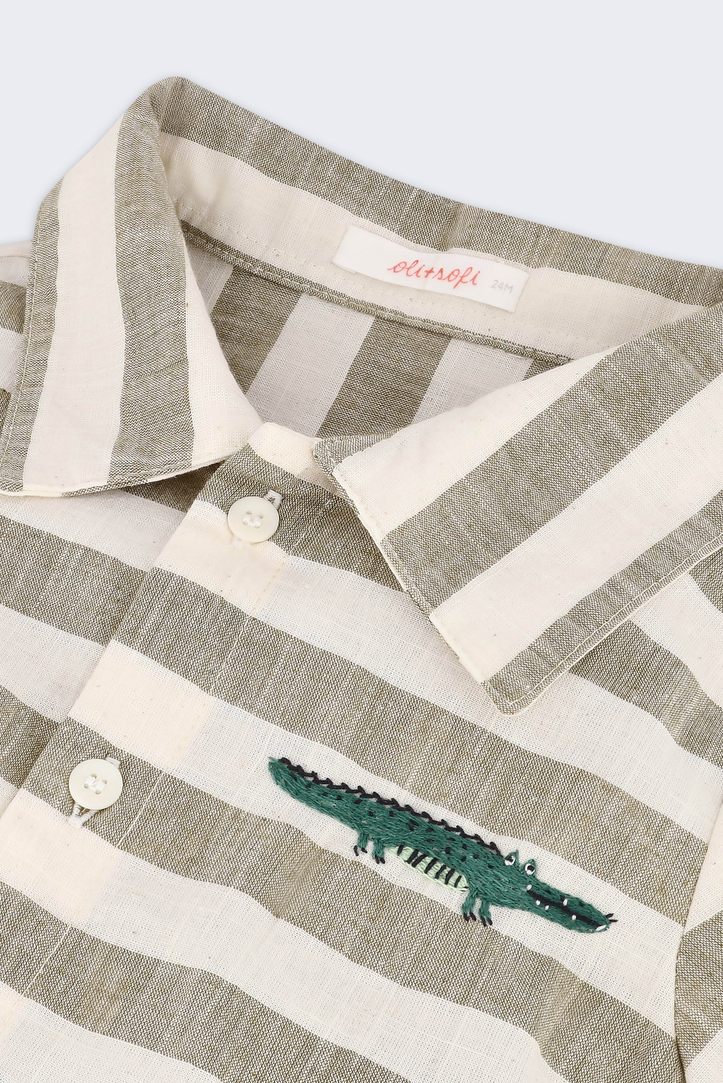 Detalhe da camisa infantil listrada verde oliva e off-white com bordado à mão de jacaré no peito e botões brancos