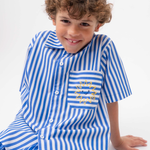 Detalhe da Camisa Gil listrada azul e branca vestida, com bolso de listras horizontais e bordado de sol amarelo.