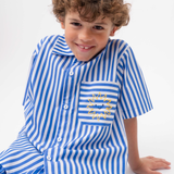 Detalhe da Camisa Gil listrada azul e branca vestida, com bolso de listras horizontais e bordado de sol amarelo.