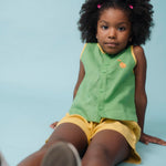 Menina usando camisa infantil verde em linho puro com bordado de cachorro caramelo, combinada com shorts amarelo