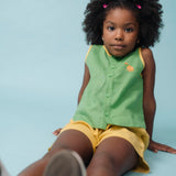 Menina usando camisa infantil verde em linho puro com bordado de cachorro caramelo, combinada com shorts amarelo
