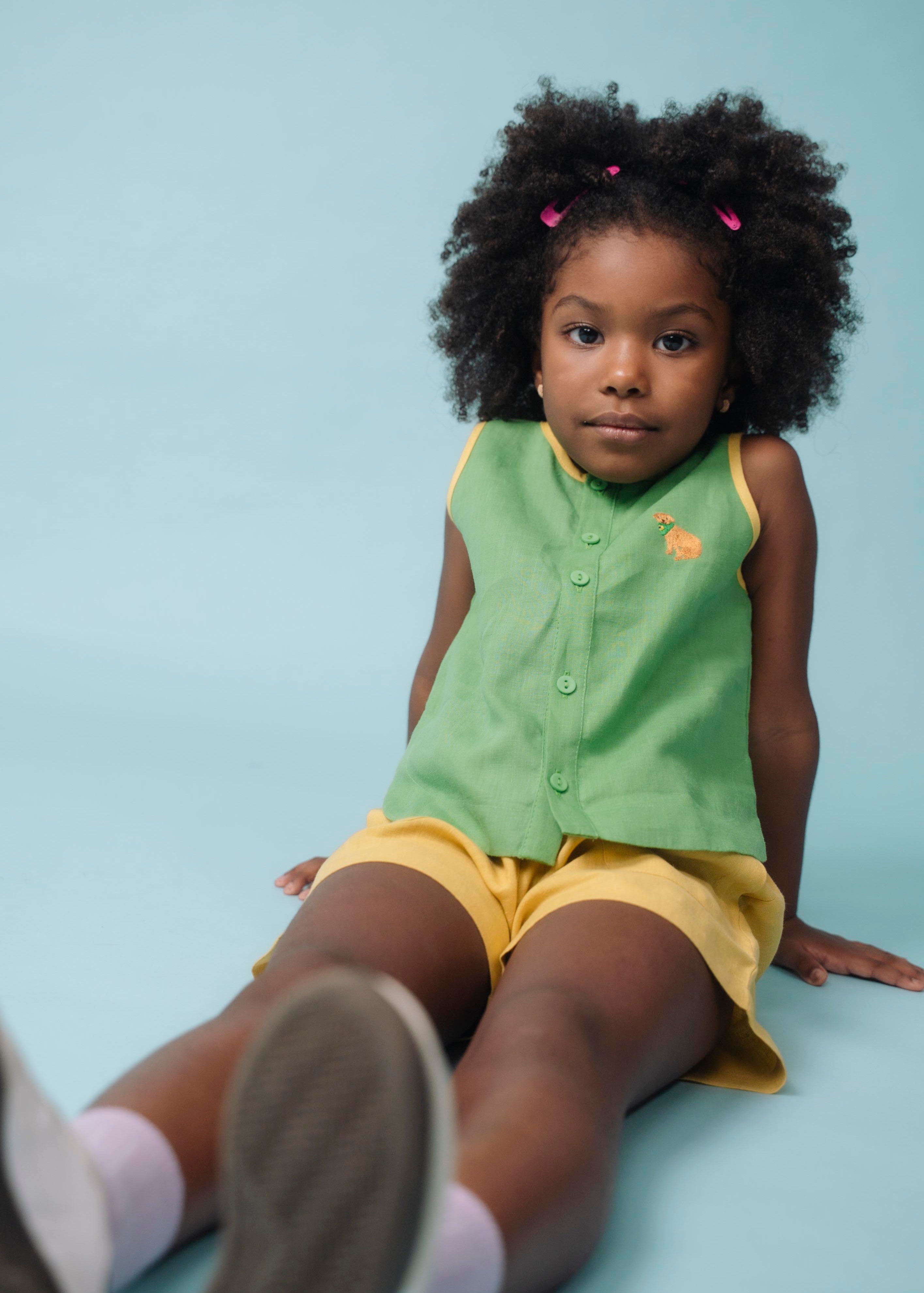 Menina usando camisa infantil verde em linho puro com bordado de cachorro caramelo, combinada com shorts amarelo