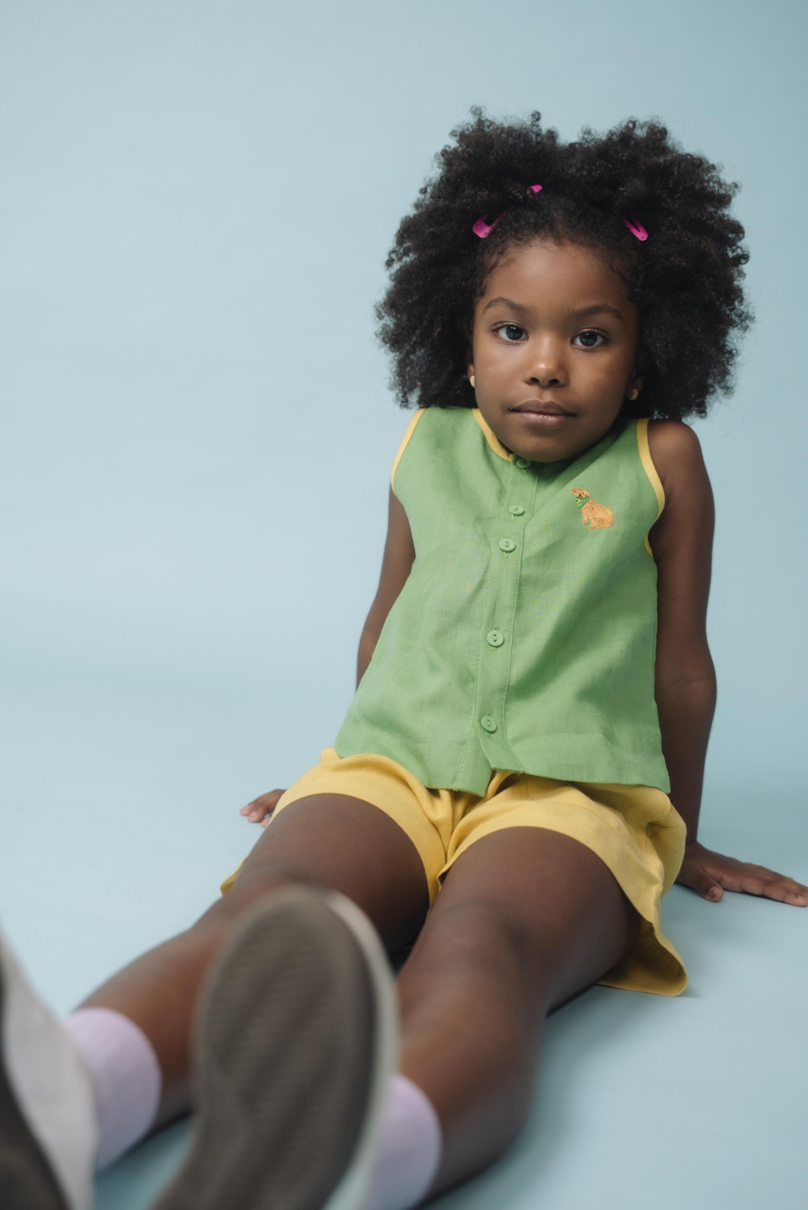 Menina usando camisa infantil verde em linho puro com bordado de cachorro caramelo, combinada com shorts amarelo