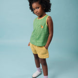 Menina usando camisa infantil em linho verde com acabamento amarelo e bordado à mão de cachorro caramelo, combinando com shorts amarelo