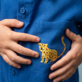 Camisa infantil azul em linho puro com gola amarela e bordado à mão de onça no bolso, usada por criança