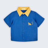Camisa infantil Tom em linho puro azul com gola amarela e bordado à mão de onça no bolso frontal, vista de frente.